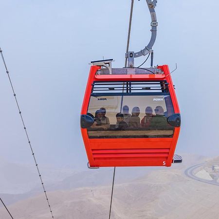 Tolip Resort El Galala Majestic Ain Sukhna Exterior foto The photo shows a red gondola lift suspended in the air, traveling along cables. Inside the gondola, a group of people can be seen. The background features a hazy landscape, possibly mountains or hills, indicating an elevated area. The scene conveys 