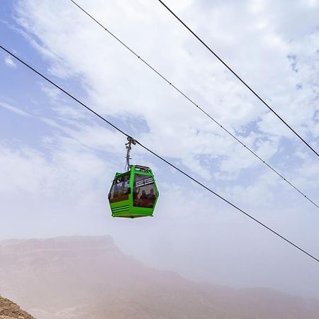 Tolip Resort El Galala Majestic Ain Sukhna Exterior foto The photo shows a green cable car suspended in the air, traveling along overhead cables. The backdrop features a hazy landscape, likely mountainous or elevated terrain, with a cloudy sky. The scene suggests a scenic transportation method, possibly us