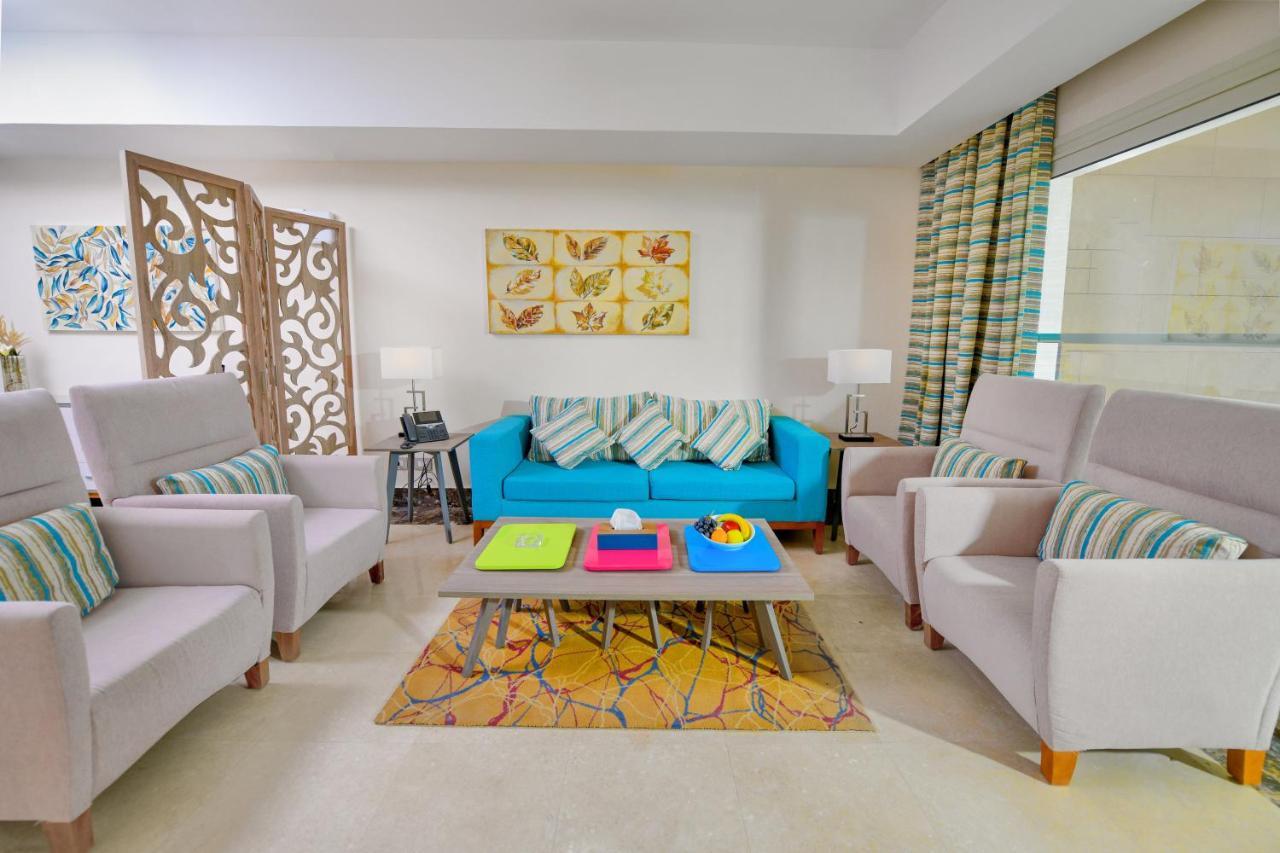 Tolip Resort El Galala Majestic Ain Sukhna Exterior foto The photo shows a stylish and colorful living room. It features a bright blue sofa with patterned cushions, complemented by two light gray armchairs. In front of the sofa, there's a wooden coffee table with vibrant trays in pink, green, and yellow. A