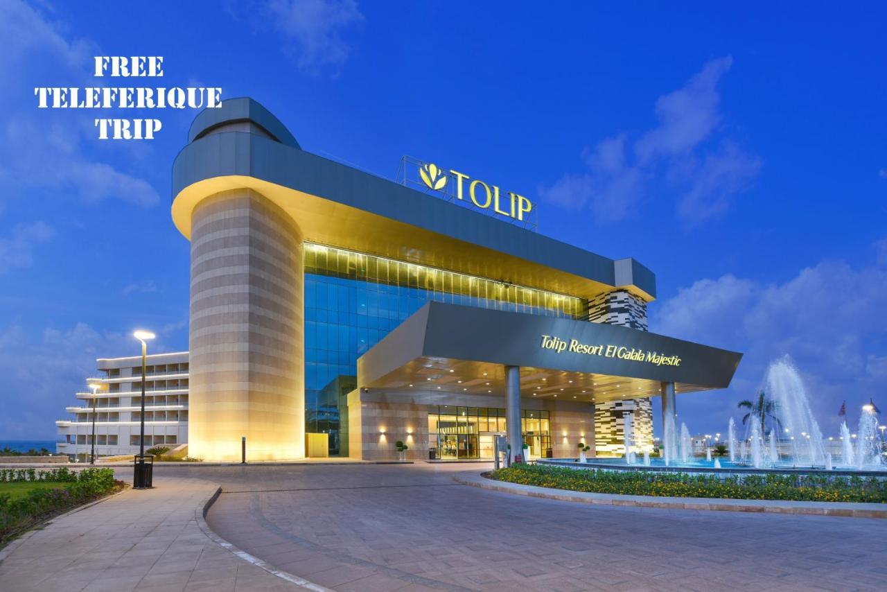 Tolip Resort El Galala Majestic Ain Sukhna Exterior foto The photo shows a modern hotel building named "Tolip Resort & Spa," featuring a sleek architectural design with large glass windows. The hotel is illuminated against a twilight sky, showcasing its prominent signage. In the foreground, there is a well