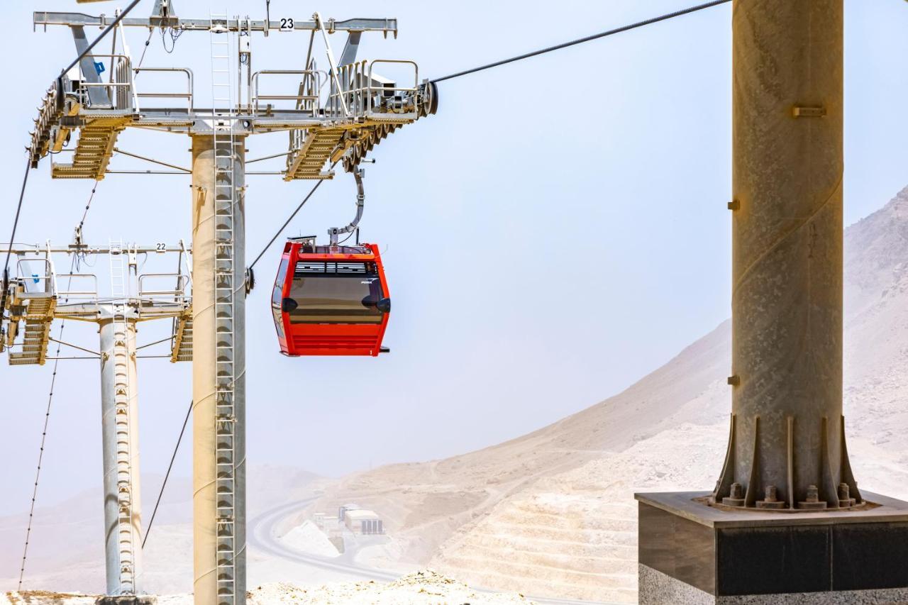 Tolip Resort El Galala Majestic Ain Sukhna Exterior foto The photo shows a cable car system with a single red gondola suspended mid-air. It appears to be part of a larger cable car infrastructure, with metal pylons supporting the cables above. The background features a hazy landscape, likely characterized 