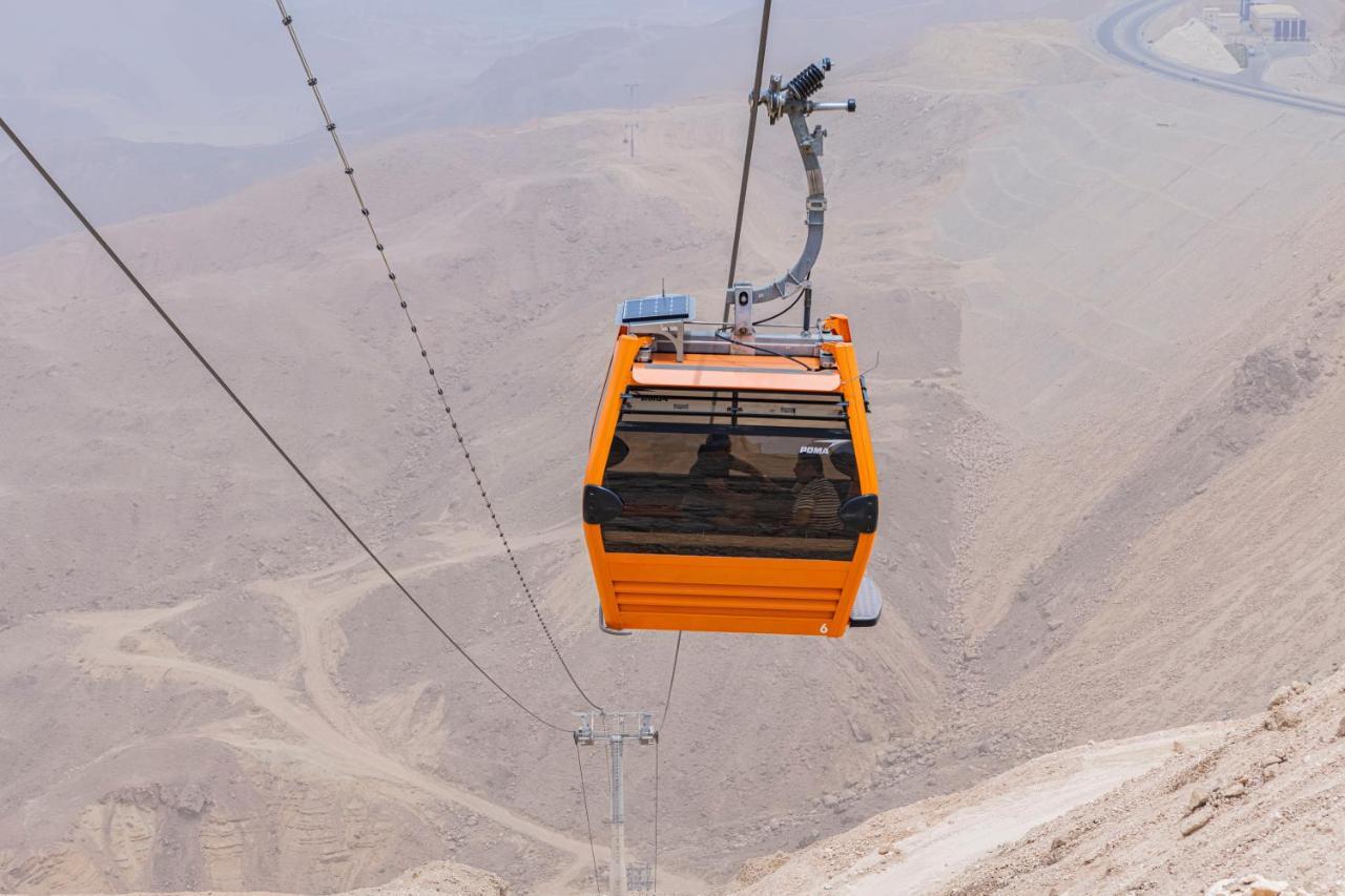 Tolip Resort El Galala Majestic Ain Sukhna Exterior foto The photo shows an orange cable car suspended in the air, traveling along a set of cables. It appears to be located in a mountainous or hilly area, with rugged terrain and dry, rocky landscapes visible below. The background features slopes that seem 