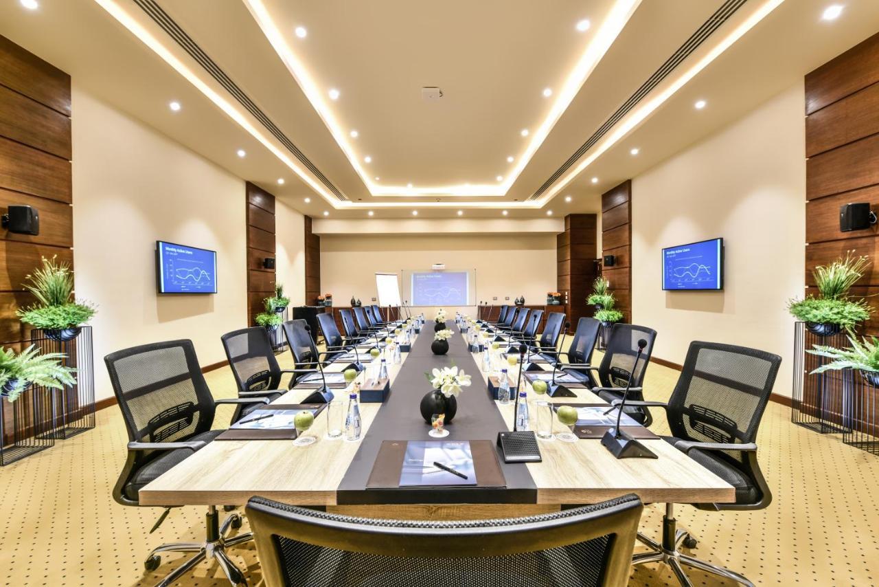 Tolip Resort El Galala Majestic Ain Sukhna Exterior foto The photo shows a modern conference room designed for meetings. It features a long rectangular table at the center, surrounded by ergonomic black chairs. The room is well-lit with ceiling lights and has a neutral color scheme. There are two large scr