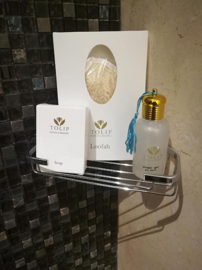 Tolip Resort El Galala Majestic Ain Sukhna Exterior foto The photo shows a small metal shelf containing three items related to personal care. 

1. **Soap**: A white box labeled "TOLIP" with the word "Soap" visible on the front.
2. **Loofah**: A package with the same "TOLIP" branding, containing loofah.
3. 